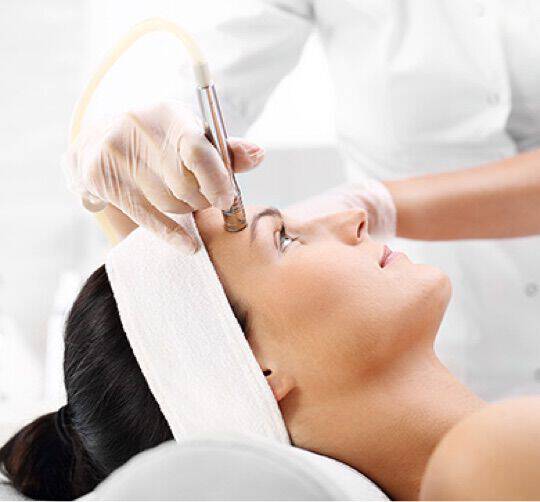En kvinne blir sett fra siden mens en lege utfører en ansiktsbehandling med et spesialisert apparat.