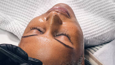 En kvinne ligger avslappet med lukkede øyne og får en ansiktsbehandling.